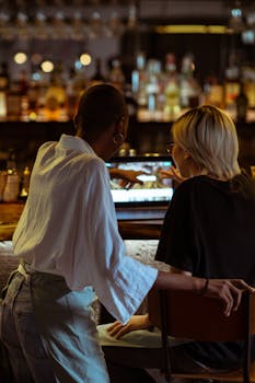 从后面可以看到，两名女子在一家舒适的咖啡馆酒吧里一起浏览笔记本电脑，气氛轻松