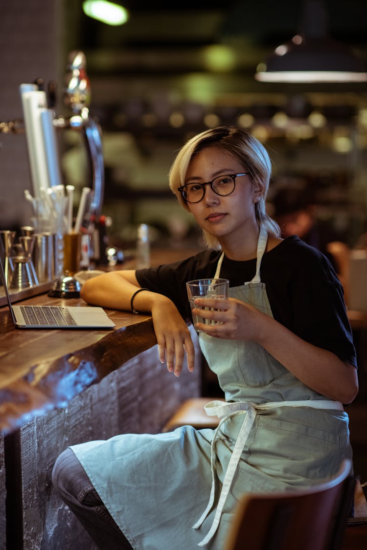 Calm Waitress In Apron With Drink And Laptop In Bar