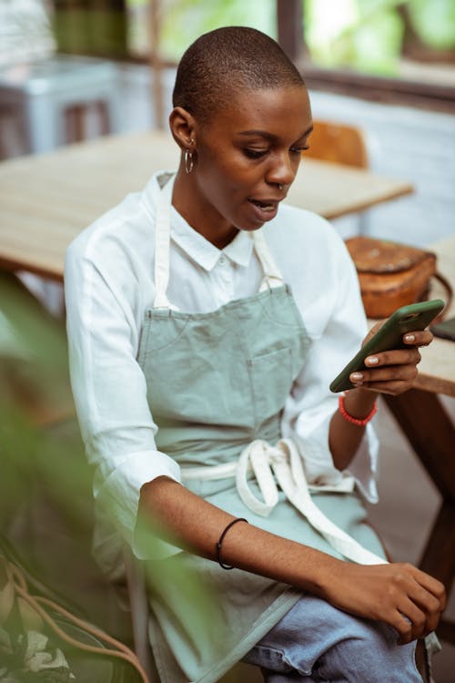 Free Surprised waitress in apron browsing smartphone Stock Photo