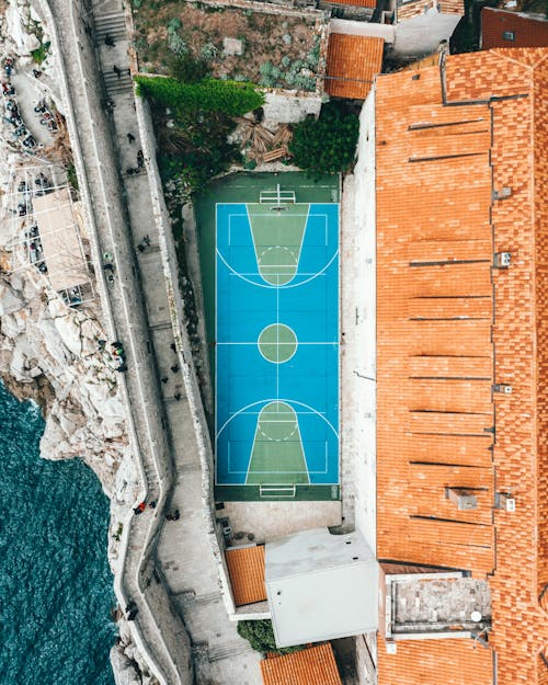 Free Aerial view of modern sports ground located between ancient building with tiled roof in old town and rocky coast of sea Stock Photo