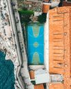 Aerial view of modern sports ground located between ancient building with tiled roof in old town and rocky coast of sea