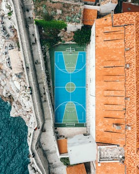 Aerial view of modern sports ground located between ancient building with tiled roof in old town and rocky coast of sea