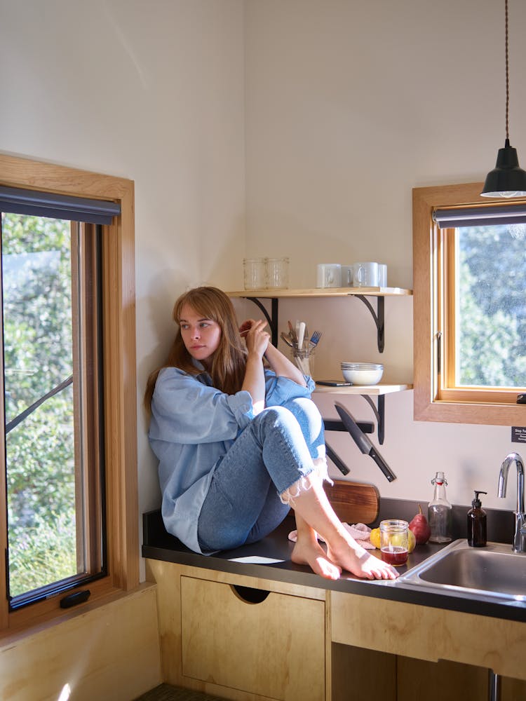 Sad Woman Sitting On Kitchen Counter And Looking Away