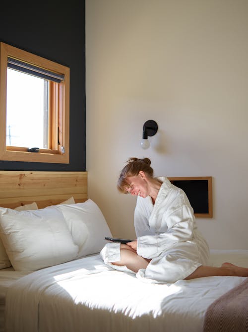 Cheerful woman in bathrobe chilling with ebook on bed