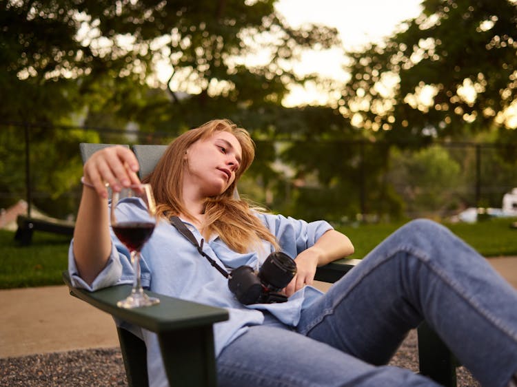 Unhappy Woman With Glass Of Wine Resting On Garden Chair