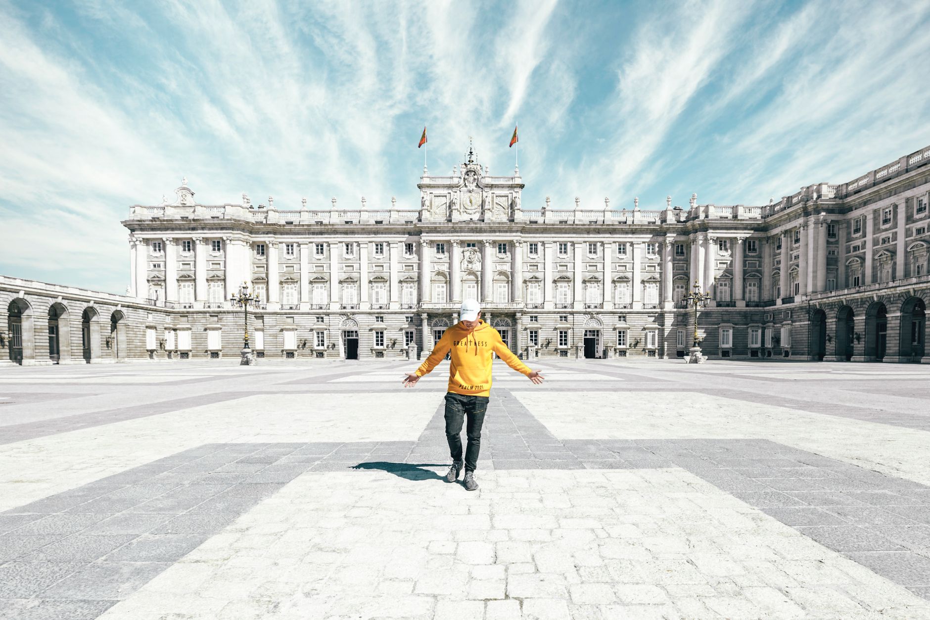 Full body of unrecognizable male traveler in casual clothes and cap standing on empty square near Royal Palace of Madrid during holiday in Spain