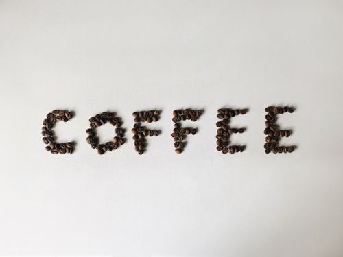 Free Creative arrangement of coffee beans spelling out 'coffee' on a white background, perfect for coffee-related themes. Stock Photo