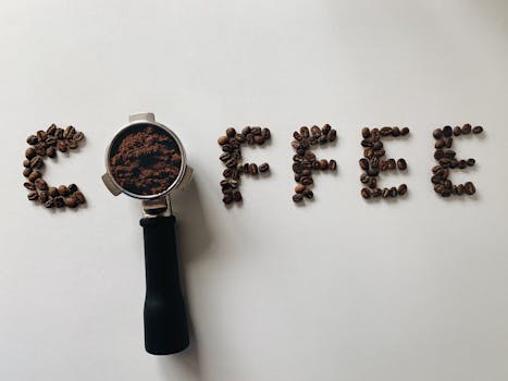 Coffee beans and portafilter creatively arranged to spell 'coffee' on a white surface.