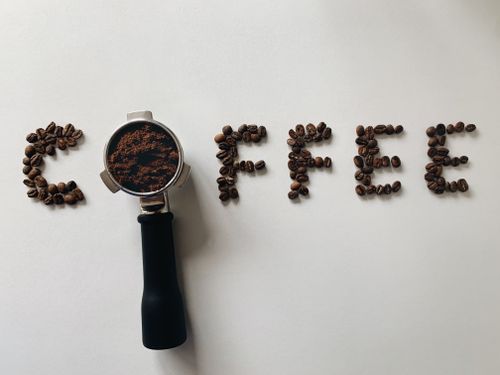 Free Coffee beans and portafilter creatively arranged to spell 'coffee' on a white surface. Stock Photo