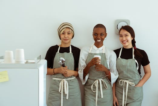 Three smiling baristas in aprons standing at the coffee counter, showcasing a friendly and professional vibe.