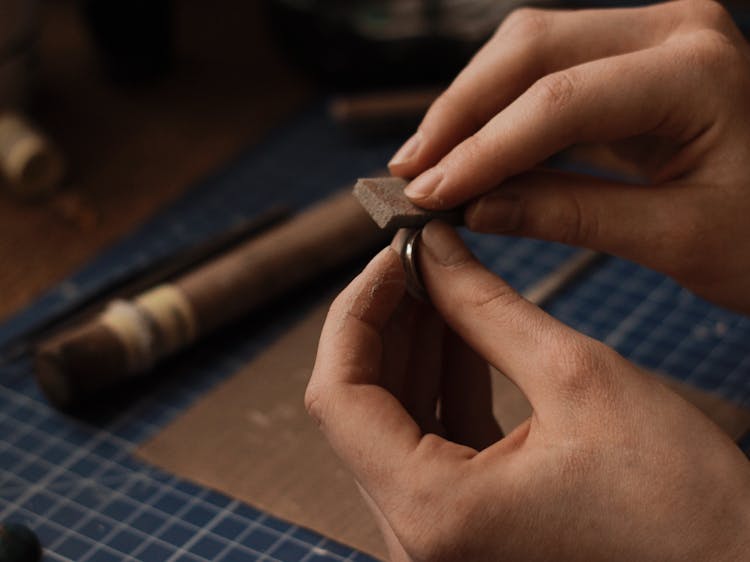 Person Holding A Silver Ring And A Polishing Tool