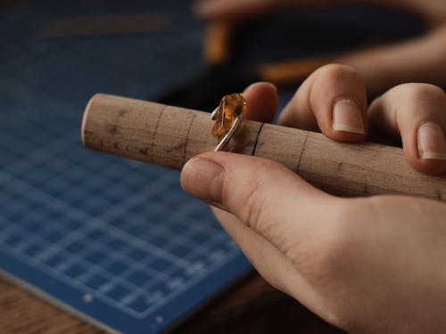 Person Holding a Silver Ring With Gemstone on a Wooden Tube