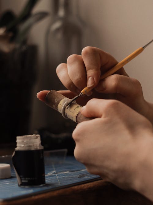 Hands of a Person Holding a Wooden Tube and a Jewelry Making Tool