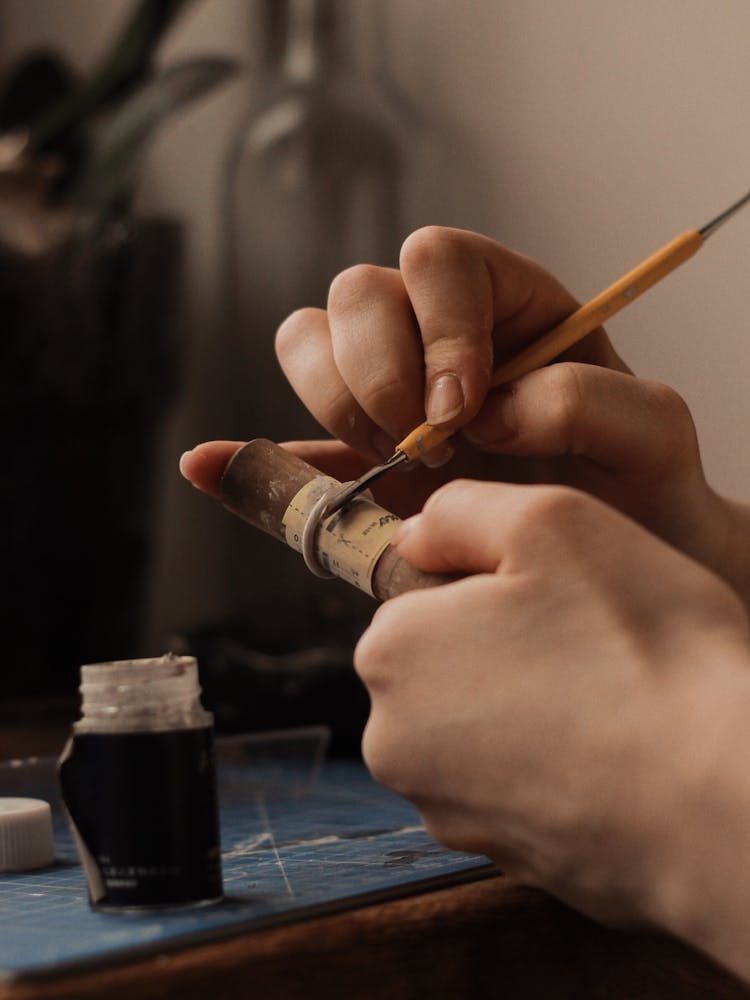 Hands Of A Person Holding A Wooden Tube And A Jewelry Making Tool