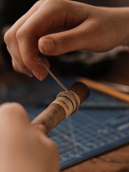 Close-up of hands skillfully wrapping a cigar in a studio setting, showcasing the art of cigar preparation.