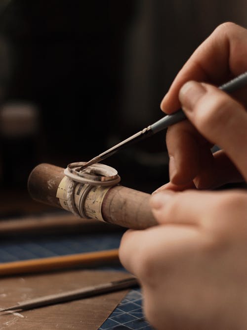 Hands of a Person Holding a Sharp Tool and a Wooden Stick With a Ring