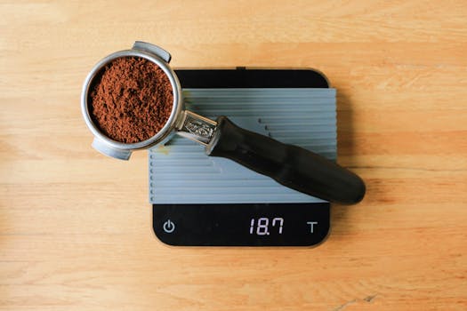 Top view of a portafilter filled with ground coffee resting on a digital scale on a wooden table.