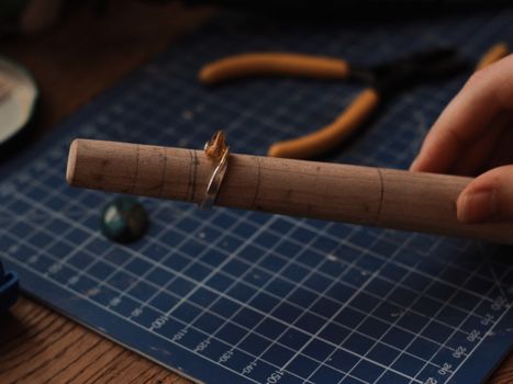 Close-up of an artisan shaping a handmade ring on a wooden mandrel tool.
