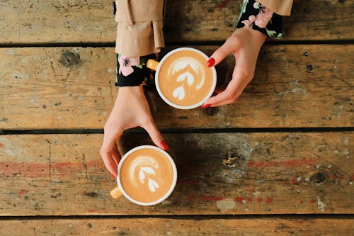 A Person Holding Ceramic Mugs on Brown Wooden Table