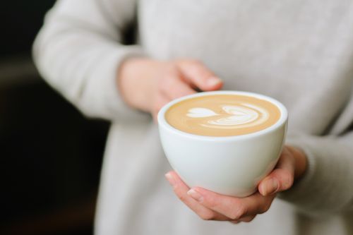 Free A close-up shot of hands holding a cup of latte with beautiful latte art. Perfect for coffee lovers. Stock Photo
