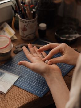 Close-up of hands creating handmade jewelry using metal clay on a work desk.