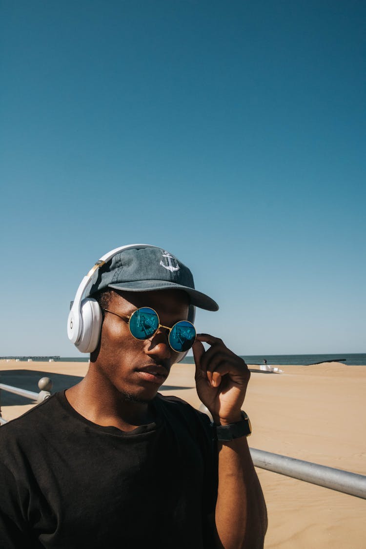 Relaxed Young Black Guy Listening To Music With Headphones On Sandy Seashore