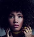 Young pensive African American female model touching curly hair and looking at camera