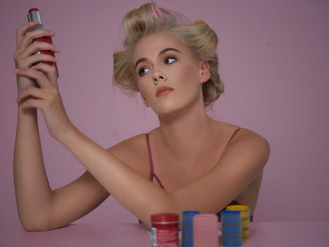 Portrait of a woman with styled hair holding a can in a studio setting, surrounded by colorful hair products.