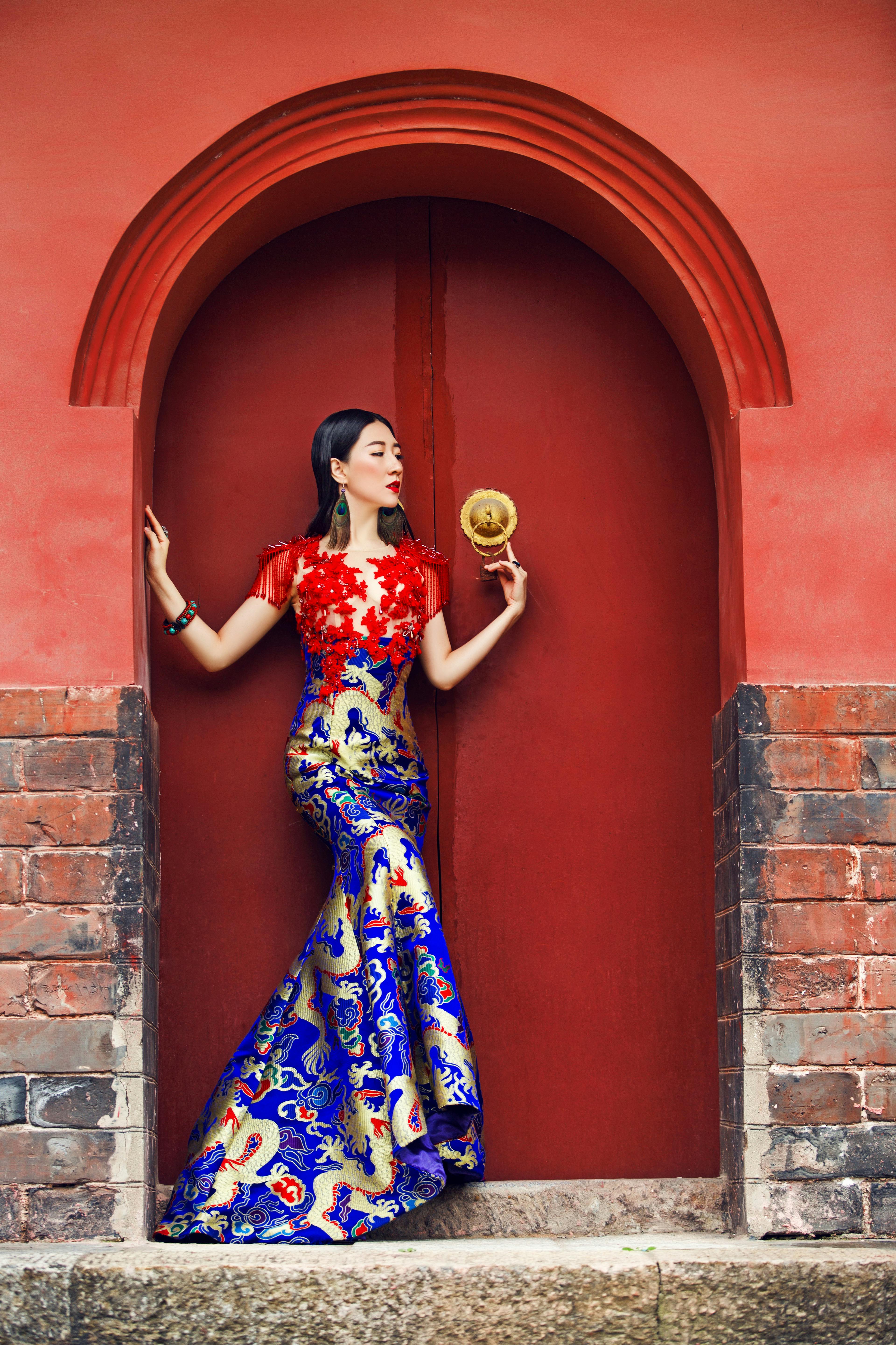 An Asian woman posing gracefully in a vibrant dress at a Chinese temple doorway.
