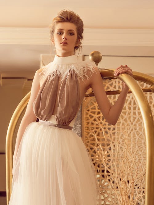 Tranquil young slim female model in elegant gown standing in dressing room and looking at camera