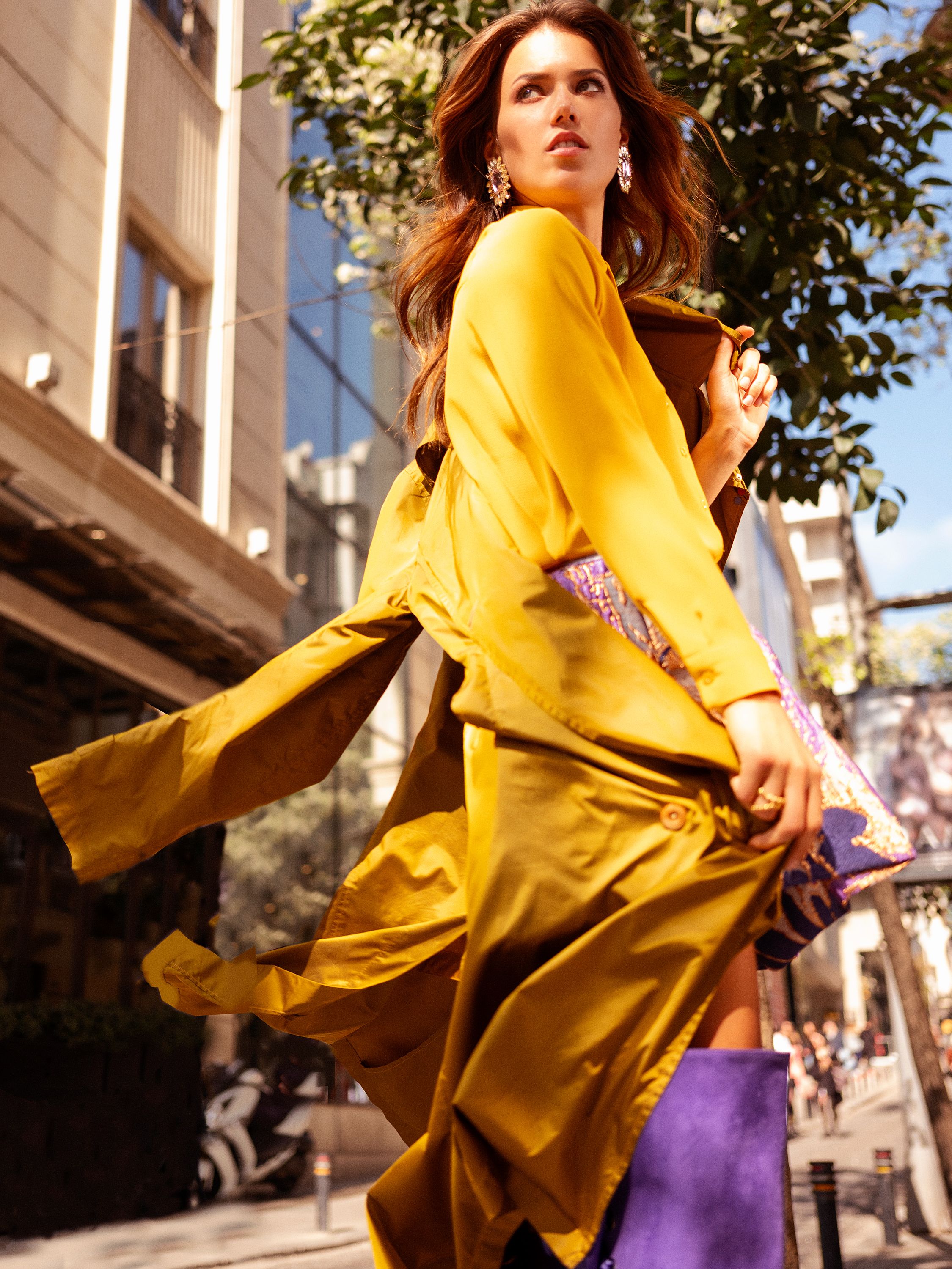 Elegant woman in motion wearing a yellow dress on a sunlit street, showcasing modern fashion.