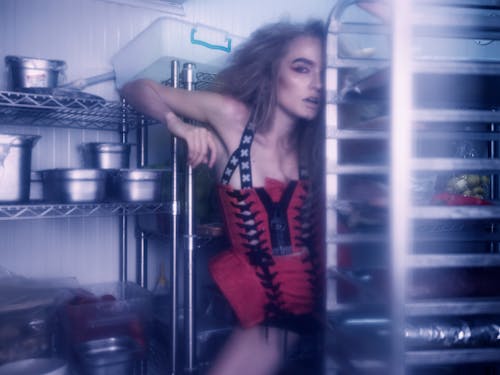 Flirting woman with bright makeup and messy hair standing between shelves in modern kitchen