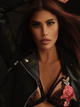 Sensual young female with makeup and flowing hair wearing black underwear and leather jacket