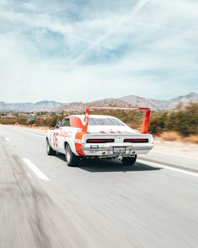 A vintage racing car speeds along a highway in California's scenic desert landscape.