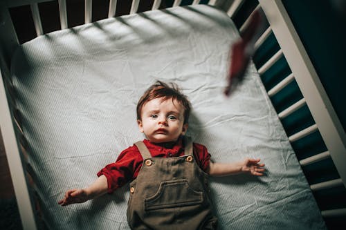 Top view of adorable baby boy with arms outstretched lying in crib during bedtime