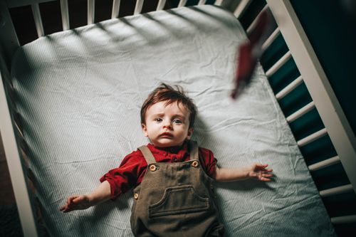 Free Top view of adorable baby boy with arms outstretched lying in crib during bedtime Stock Photo