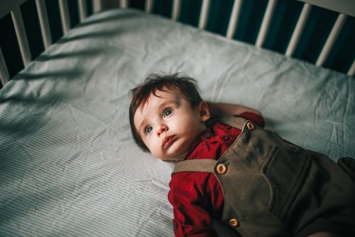Free From above of adorable baby with plump cheeks looking away while lying on soft bed Stock Photo