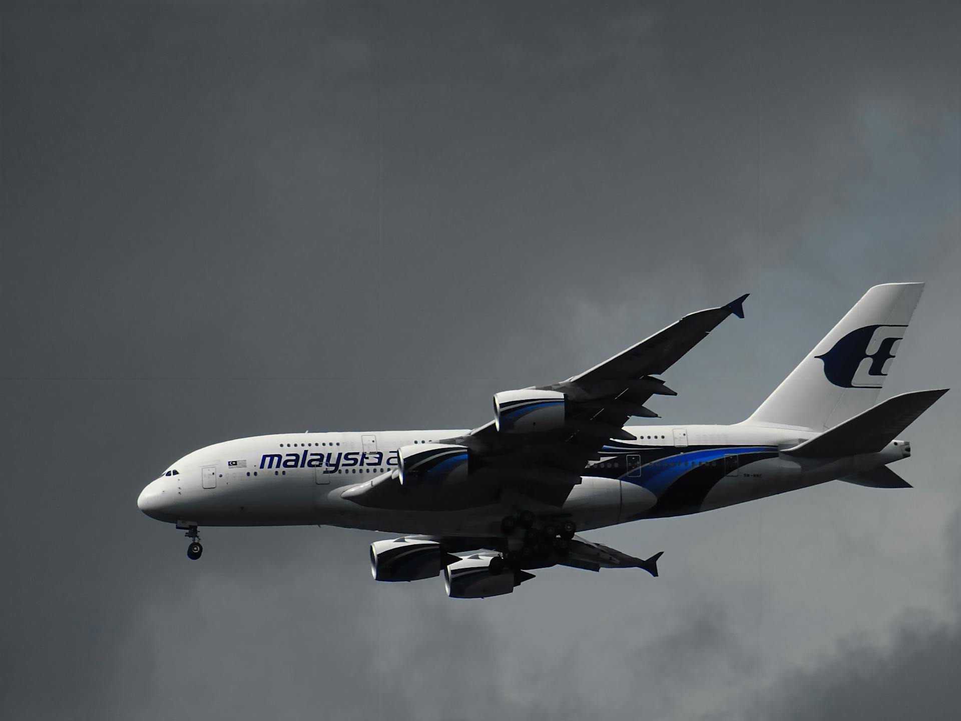 An Airbus A380 from Malaysia Airlines cruising through dark, cloudy skies.