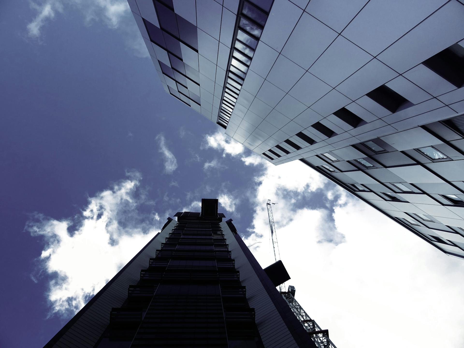 Low angle view of modern skyscrapers with a construction crane and clouds in the sky.