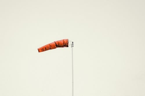 Red windsock on pole against gray sky