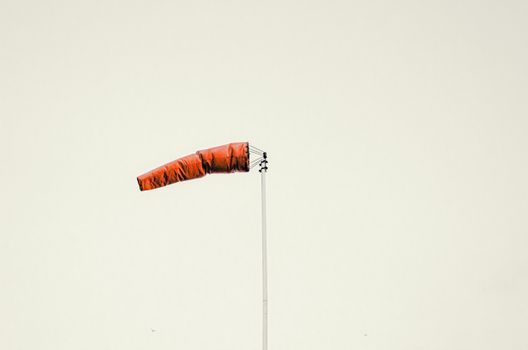 Red windsock on pole against gray sky