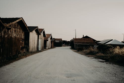Empty rural road covered with snow going through village with shabby wooden houses on cloudy winter day