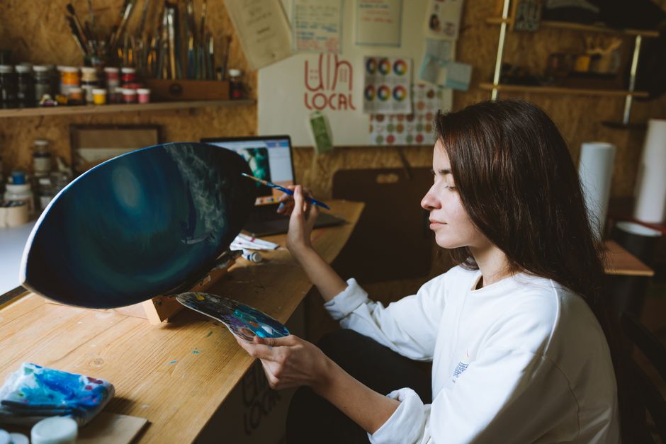 Norton VPN vs Surfshark: Which Bundled Antivirus+VPN Protects Better? A woman artist painting a skateboard in her home studio. Creative workspace with brushes and paints.