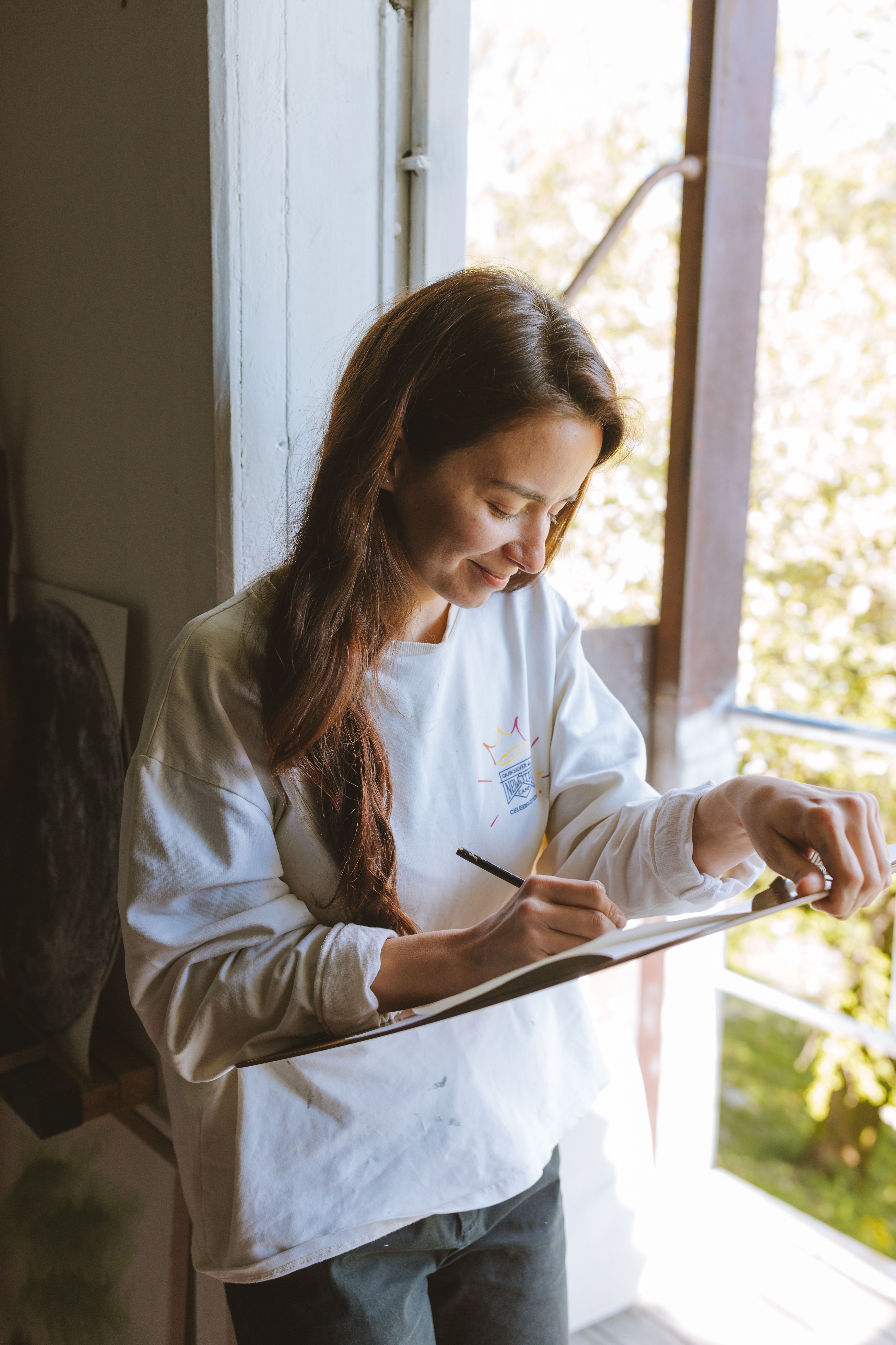 A Woman Smiling While Writing on a Clipboard · Free Stock Photo