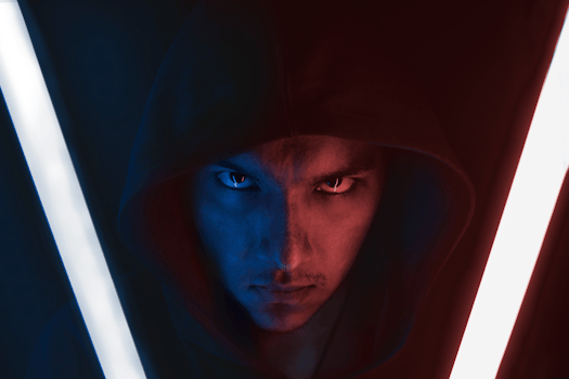 Intense close-up portrait of a man in a hoodie under red and blue neon lights.