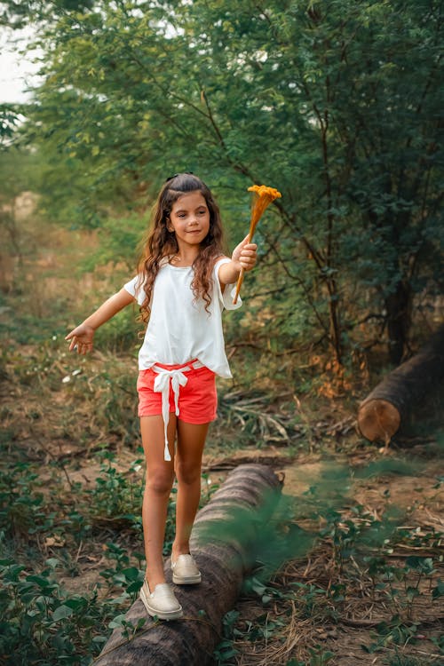 Girl in White Shirt and Red Shorts Holding Orange Flower