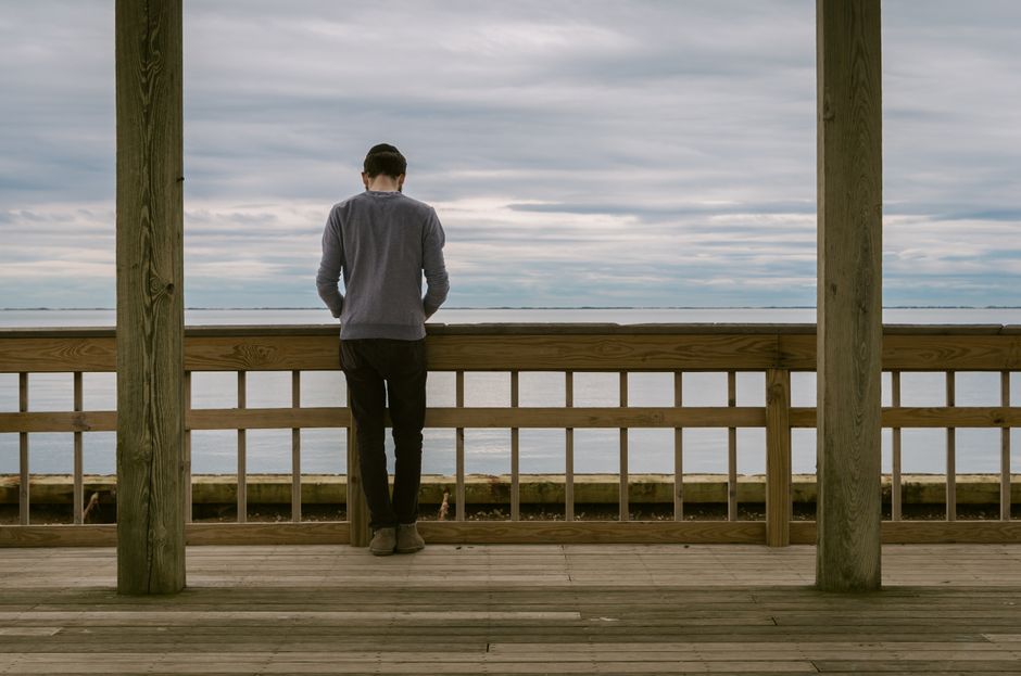 Man standing on a wooden deck, gazing at the cloudy ocean view, conveying serene solitude.
