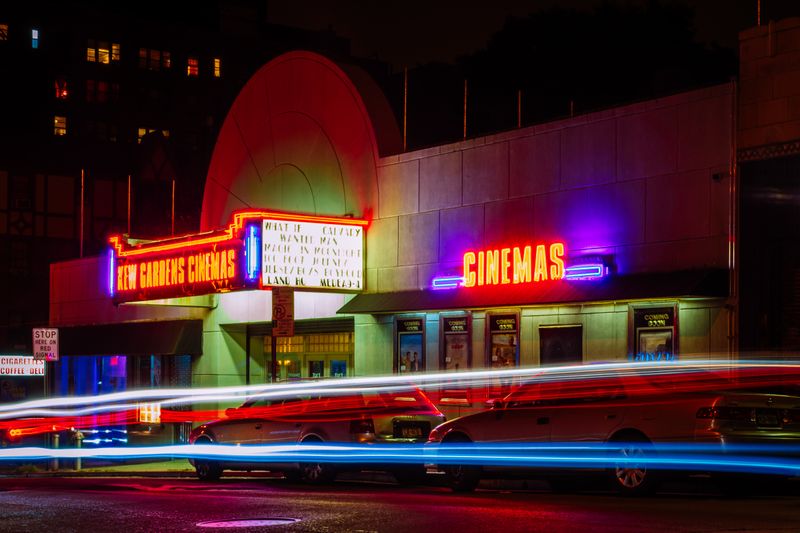 Vibrant night view of New Gardens Cinemas in Queens, New York with colorful neon lights and light streaks.