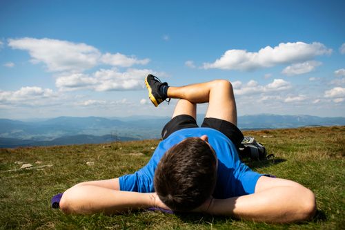 Free Unrecognizable young male athlete in sportswear lying on grassy ground in mountainous terrain and resting after outdoor workout Stock Photo