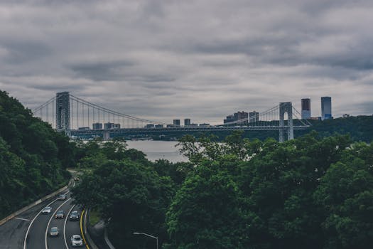 城市河流上的吊桥横跨在阴云密布的天空下，桥上有汽车驶过，远处是城市的天际线